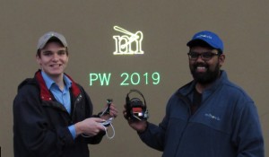 Daniel Lovell left holds a green PZ-02 Playzer Module displaying PW 2019 while Abhishek Kasturi right showcases the programmable light system PLS projecting the Mirrorcle M logo This unprecedented visibility and contrast despite outdoor, daylight conditio